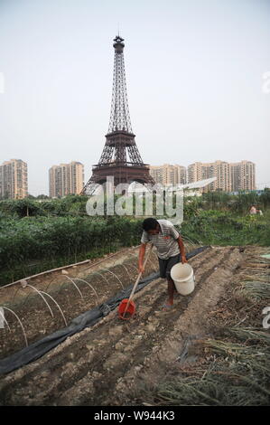 Ein chinesischer Bauer bewässert sein Feld in der Nähe der Hälfte - sortierte Kopie des Eiffelturms an Tianducheng, eine kleine chinesische Gemeinschaft Paris repliziert, in Hangzhou Stockfoto