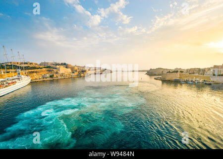 Sonnenaufgang am Grand Harbour von Valletta Malta mit Sun schlagen die alte Stadt und ein kleines Kreuzfahrtschiff Stockfoto