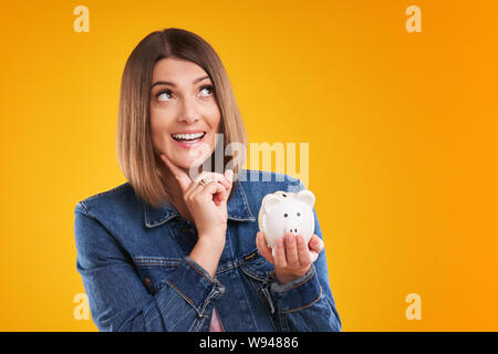 Nahaufnahme der Frau in Jeansjacke holding Sparschwein auf gelbem Hintergrund Stockfoto