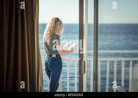 Blonde Frau mit einem Buch vor dem Meer Stockfoto