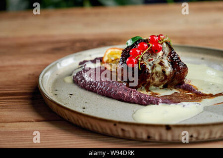 Nahaufnahme des leckeres Stück Grill bleiben auf Platte mit Gemüsebrei, Moosbeere, Minze und Zitrone. Köstliches Essen im Restaurant am Abend gekocht. Konzept der Küche und essen. Stockfoto