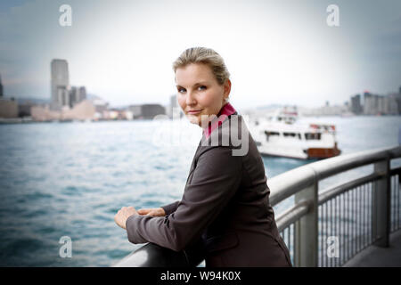 Porträt einer zuversichtlich, Mitte - Erwachsene business Frau auf ein Geländer an einer Uferpromenade gelehnt neben einem Hafen. Stockfoto