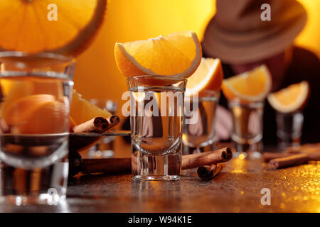 Gläser gold Tequila mit Orange und Zimt Sticks auf einen Tisch in der Bar. Trinken Mann in einen Hut an der Bar. Selektive konzentrieren. Stockfoto