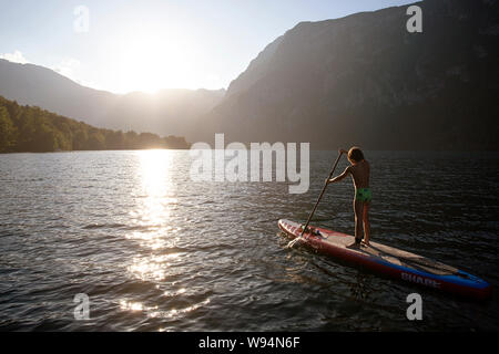 Junge paddeln auf Sup, Erholung an der smaragdgrünen Quellwasser von alpinen See Bohinj, Slowenien bei Sonnenuntergang Stockfoto