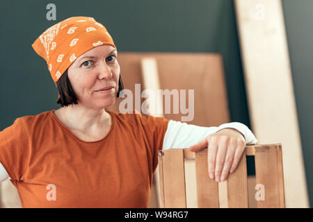 Stolz Frau Carpenter mit fertigen Holzkiste in ihrem kleinen Geschäft Holzarbeiten workshop Posing Stockfoto