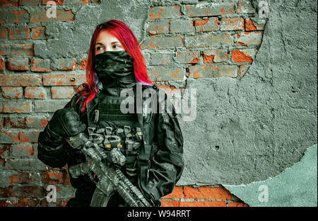 Rot - Haar Frau in Uniform mit Maschinengewehr auf Ziegel Wand Hintergrund Stockfoto