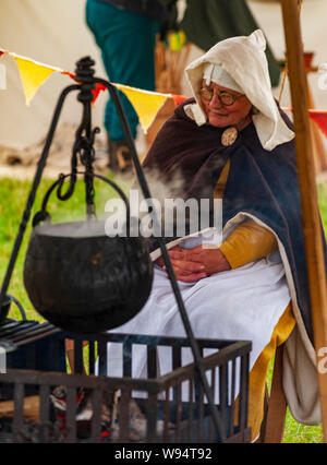 Re-enactors Phase der Schlacht von Shrewsbury 1403 auf dem Original Battlefield im Juli 2019 Frau in Mittelalterliches Kleid im Camp mit Kessel Stockfoto