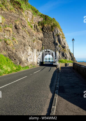 Black Arc Tunnel und Causeway Coastal Route. Malerische Straße entlang der östlichen Küste des County Antrim, Nordirland, Großbritannien. Luftaufnahme im Sonnenaufgang Licht Stockfoto