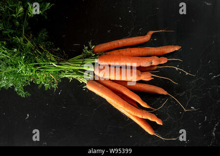 Bündel organische rohe Karotte mit grünen Blättern auf dem Schwarzen Brett, Ansicht von oben Stockfoto