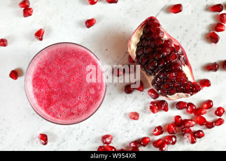 Glas mit rosa Granatapfel Smoothie, mehr Beeren und ein Stück Obst am weißen Stein Brett daneben, Ansicht von oben Stockfoto