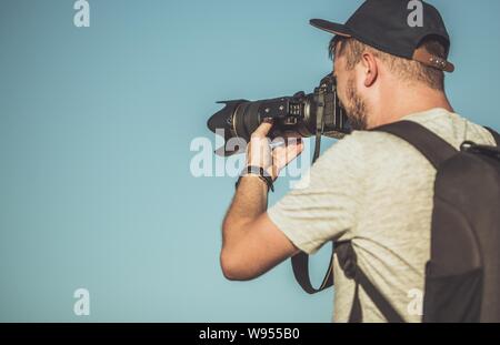 Kaukasische Fotograf mit Teleobjektiv angebracht, um die modernen DSLR-Kamera. Leidenschaftlich über Fotografie. Professionelle Ausrüstung. Stockfoto