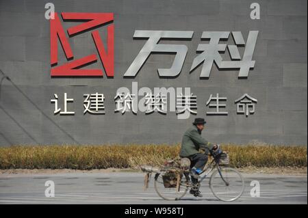 ---- Ein Mann fährt mit dem Fahrrad hinter dem Logo der China Vanke in der Stadt Shenyang, Provinz Liaoning im Nordosten Chinas, den 6. April 2012. China Vanke Co, die Coun Stockfoto