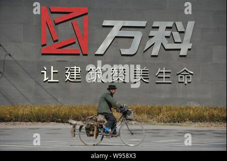---- Ein Mann fährt mit dem Fahrrad hinter dem Logo der China Vanke in der Stadt Shenyang, Provinz Liaoning im Nordosten Chinas, den 6. April 2012. China Vanke, das Land Stockfoto