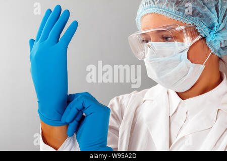 Im Labor, eine Wissenschaftlerin Chemiker setzt auf Schutzhandschuhe. Mikrobiologe in sterilen Kleidung und Schutzbrille. Stockfoto