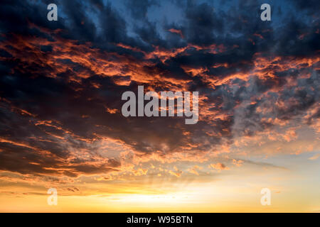 Dunkle Gewitterwolken mit rot orange Reflexionen der untergehenden Sonne. Malerische Gewitterwolken beleuchtet durch die letzten Strahlen der untergehenden Sonne. Dramatische cloudscape. Stockfoto
