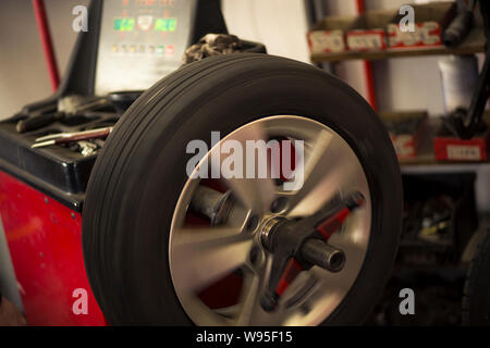 Autoreifen werden in der Garage wegen der Wintersaison gewechselt. Arbeitsplatzumgebung in dunklen Farben, drehbar, Montage des Reifens auf der Felge. Stockfoto