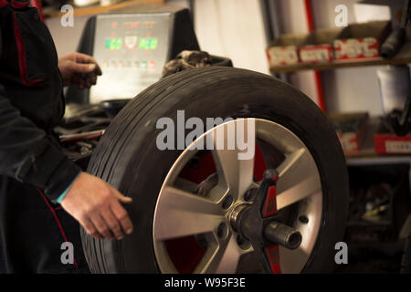 Autoreifen werden in der Garage wegen der Wintersaison gewechselt. Arbeitsplatzumgebung in dunklen Farben, drehbar, Montage des Reifens auf der Felge. Stockfoto