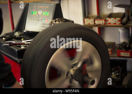 Autoreifen werden in der Garage wegen der Wintersaison gewechselt. Arbeitsplatzumgebung in dunklen Farben, drehbar, Montage des Reifens auf der Felge. Stockfoto