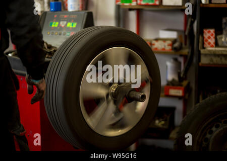 Autoreifen werden in der Garage wegen der Wintersaison gewechselt. Arbeitsplatzumgebung in dunklen Farben, drehbar, Montage des Reifens auf der Felge. Stockfoto