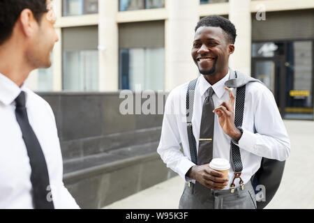 Happy afrikanischen Geschäftsmann holding Tasse Kaffee im Gespräch mit seinem Kollegen und lächelnd, während man im Freien Stockfoto