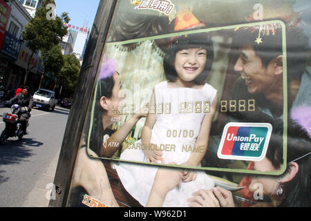 ---- Ein chinesischer Radfahrer reitet ihr Elektrofahrrad Vergangenheit eine Werbung für Kreditkarten mit dem Logo der China UnionPay in Nantong City, East China Stockfoto