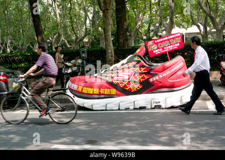 Fußgänger Spaziergang, vorbei an einem riesigen Sneaker der Slogan, verbrennen Kalorien statt Benzin Lager, auf einer Straße in Shanghai, China, 12. September 2012. A h Stockfoto