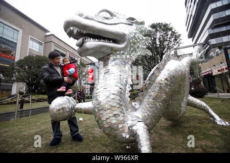 Ein Mann sein baby Holding steht neben einem Drachen aus Abfällen CDs und DVDs bei Shopping Plaza in Shanghai, China, 8. Januar 2012. Die chinesische Luna Stockfoto