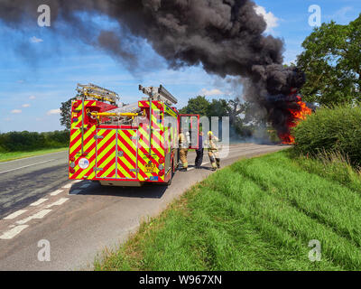 Schwarzer Rauch weht über einer Hauptstraße als Besatzungen von Lincolnshire Fire and Rescue kommen, um ein landwirtschaftliches Fahrzeug anzugehen Feuer Stockfoto