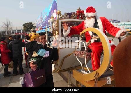 Ein junger chinesischer Mann gekleidet in einem Santa Claus kostüm Wellen für Fußgänger wie er fährt einen Schlitten Geschenke zu verteilen Weihnachten in Hainin zu feiern. Stockfoto