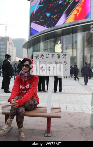 Eine junge chinesische Frau, die neben einem Plakat mit Schildern mit der Aufschrift sitzt, mein Mann nicht zuverlässig ist, er mich nicht ein iPhone kaufen 5, ich bin auf der Suche nach einem reichen m Stockfoto