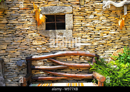 An der Wand eines ländlichen Herbst Haus mit einem kleinen Fenster, eine Holzbank und eine Ernte. Haus im Dorf Blätter fallen. Stockfoto