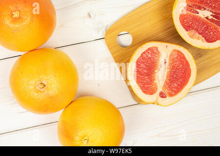 Gruppe von drei ganzen zwei Hälften von frischem rosa Grapefruit auf Bambus Schneidebrett flatlay auf weißem Holz Stockfoto