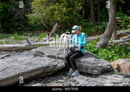 Weibliche Wanderer mit Hund ruht auf einem großen Felsen Stockfoto