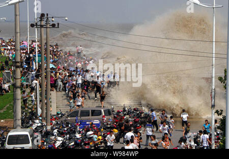 Besucher und Anwohner wie Wellen aus einem Gezeiten laufen Bohrung Schwankung hinter einer Barriere am Ufer des Qiantang Fluss in Hangzhou City, East China Zhejiang Stockfoto