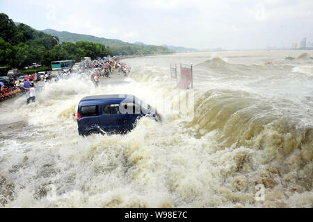 Besucher und Anwohner wie Wellen aus einem Tidal Bore Schwankung hinter eine Absperrung und ein Fahrzeug am Ufer des Qiantang Fluss in Hangzhou City, East C Stockfoto