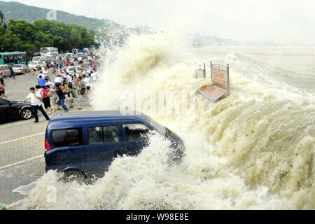 Besucher und Anwohner wie Wellen aus einem Tidal Bore Schwankung hinter eine Absperrung und ein Fahrzeug am Ufer des Qiantang Fluss in Hangzhou City, East C Stockfoto