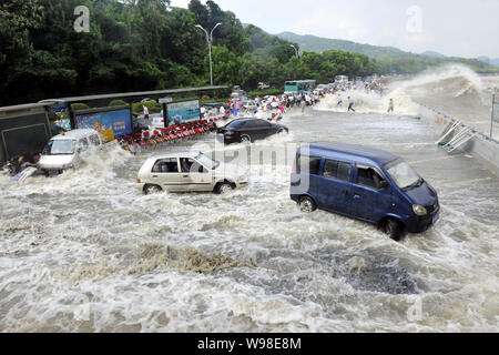 Besucher und Anwohner wie Wellen aus einem Tidal Bore Schwankung hinter eine Absperrung und Fahrzeuge am Ufer des Qiantang Fluss in Hangzhou City, Ost-CH Stockfoto