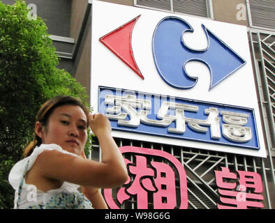 ---- Eine chinesische Frau geht vorbei an der Beschilderung von Carrefour auf einer Straße in Shanghai, China, 30. Juni 2011. Europas größter Einzelhändler Carrefour auf Di Stockfoto