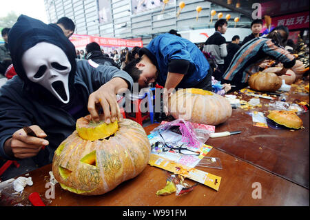 Ein junger Mann in einer ghost Kostüm und andere Teilnehmer gekleidet machen Kürbis Laternen bei einem Wettbewerb zu Hallowmas in Wuhan City, zentrale Feiern Stockfoto