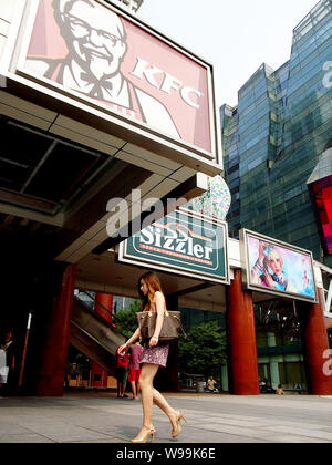 ---- Eine trendige junge chinesische Frau geht hinter einem KFC-fast-food-restaurant in Peking, China, 17. Juli 2010. Colonel Sanders ist eine Ikone der amerikanischen Br Stockfoto