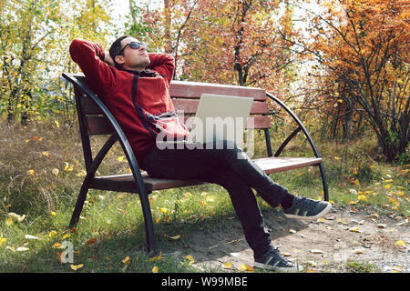 Eine entfernte Mitarbeiter, Freelancer auf dem Hintergrund der Herbst Park. Junge Unternehmer sitzt im Park und mit Laptop. software engineer mit Laptop Stockfoto