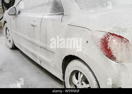 Auto ist mit weißen Schaum im Auto waschen in der Garage abgedeckt. Self-Waschmaschine. Automatische Autowäsche. Stockfoto