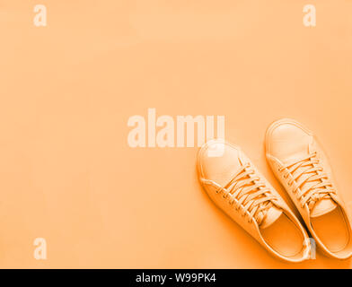Orange Leder Sneakers auf pastellorange Hintergrund, Monochrom. Paar orange Sport Schuhe mit Kopie Platz für Text oder Design. Top View oder flach Stockfoto
