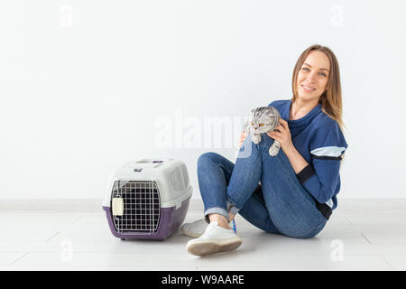 Charmante positive junge Frau hält in ihrer Hände ihre schönen grauen schottischen Katze sitzt auf dem Boden in eine neue Wohnung. Pet-Konzept. Stockfoto