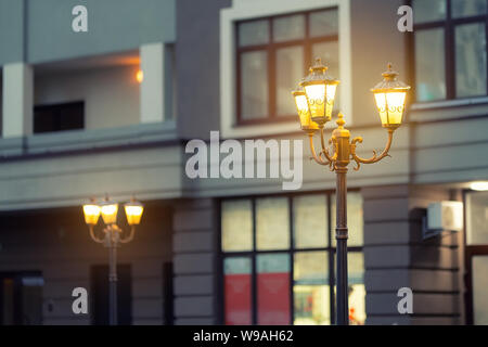 Schöne klassische Metall Straßenlaterne in Abend gegen modernes Gebäude in Abend. Warmes Licht Eisen retro Laterne an Ort Straße in der Dämmerung. Stockfoto