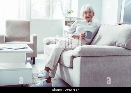 Schön angenehm Großmutter saß auf beige Sofa im Wohnzimmer Stockfoto