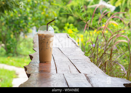 Eiskaffee im Glas auf dem Tisch Hintergrund Pennisetum pedicellatum und Baum. Stockfoto
