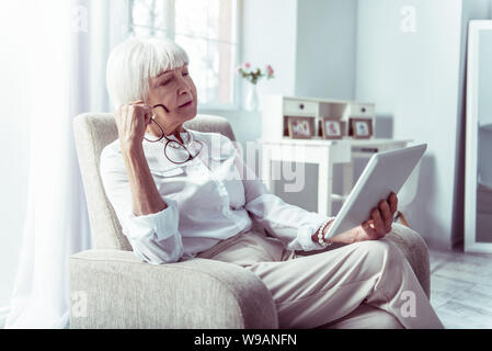 Blonde ältere Dame Gefühl nachdenklich Lesen lokale Nachrichten auf Tablet Stockfoto