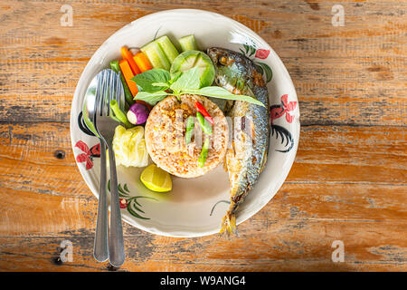 Gebratener Reis mit Chili würzig mit Fisch und Gemüse in Weiß Platte auf dem Holztisch. Stockfoto