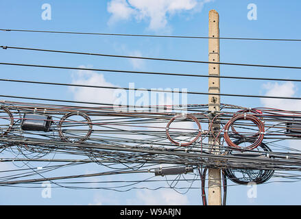 Elektrische Leitungen und Kabel hängend auf einer konkreten Säule und den strahlend blauen Himmel. Stockfoto